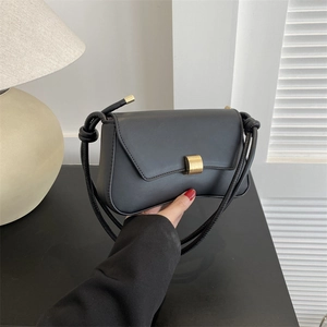 Minimalist black leather baguette bag with geometric gold clasp and knotted shoulder strap