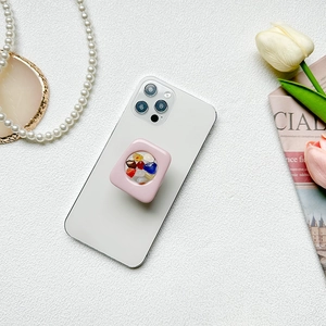 Detailed view of a pink square phone grip with colorful gemstones on a white phone
