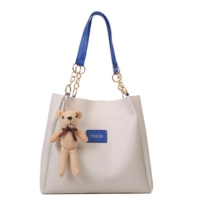 Chic cream tote bag with blue handles, gold chain detail and a small knit bear pendant