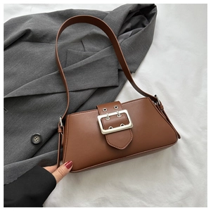 Detail of a brown leather underarm bag featuring a wide silver buckle and matte texture