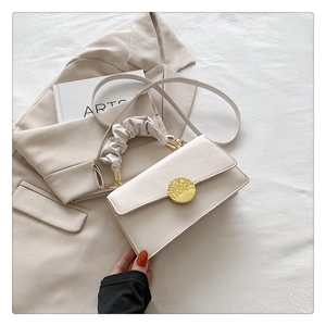 Détail du sac bandoulière crème avec boucle dorée et poignée plissée sur tissu