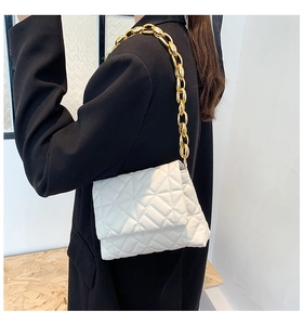 Detail of white quilted faux leather handbag with bold golden chain strap on model shoulder