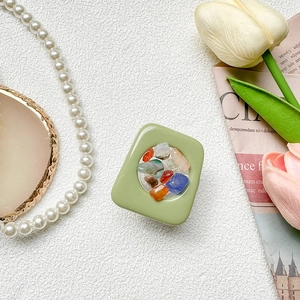 Detail view of olive green phone grip with colorful gemstone inlay on white texture background