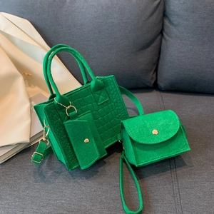 Three-piece green felt handbag set with crocodile pattern on a gray fabric sofa