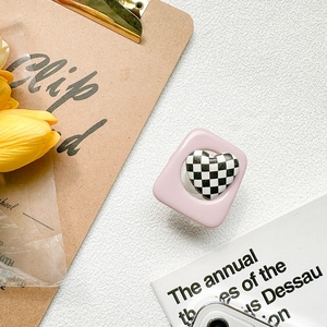 Close-up of pink heart-shaped checkerboard phone grip on a white textured background
