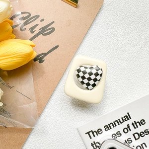 Detail of cream square phone grip with black and white checkered heart on white surface