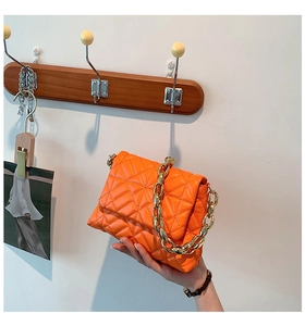 Close-up of bright orange quilted bag featuring a chunky gold chain handle and soft PU texture