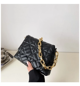 Detail of black quilted faux leather handbag featuring a chunky gold acrylic chain strap