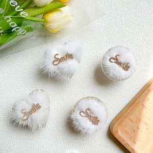 Detail of four white plush hair clips with gold diamond Smile lettering and heart shape
