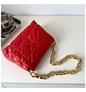 Macro detail of red quilted shoulder bag with bold gold acrylic chain strap and soft texture