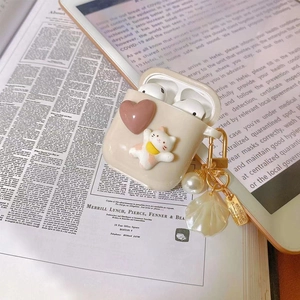 Detail of cream AirPods case with cat, heart charm, pearls, and shell pendant