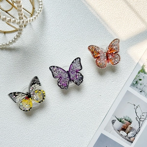 Three glittering butterfly phone grips in yellow, purple, and orange on leather texture
