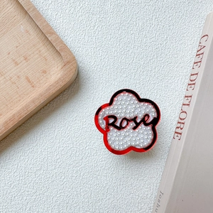 Détail du support téléphone en fleur rouge avec perles et texte Rose dans un décor