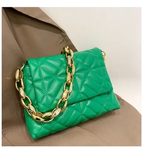 Close-up of green quilted shoulder bag with decorative thick gold chain on a blazer