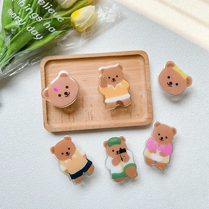 Cute brown bear acrylic phone griptok set with various outfits on a wooden tray