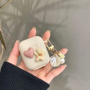 Detail of cream AirPods case with 3D pink heart, cat charm, and pearl shell keychain