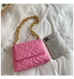 Detail shot of pink quilted PU shoulder bag with thick gold chain on a textured surface