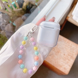 Clear AirPods case with pastel bead bracelet handle held against a soft outdoor background