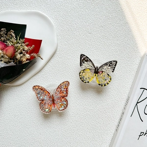 Detail of butterfly phone grip featuring flowing star sequins in orange and yellow