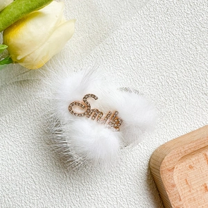 Detail of soft white plush phone grip featuring a gold rhinestone Smile logo accent