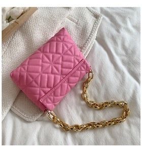 Detail of pink quilted flap shoulder bag with chunky gold acrylic chain on soft bedding