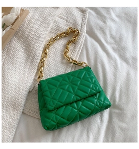 Detail of green quilted handbag with chunky gold chain strap on soft white fabric