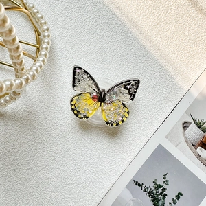 Macro shot of butterfly-shaped phone grip with glitter and yellow-black liquid sand