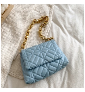 Close-up of light blue quilted handbag featuring a bold gold chain and geometric texture