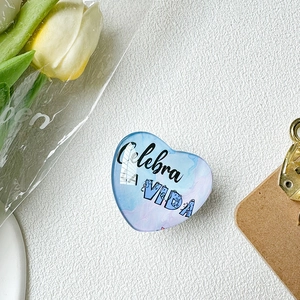 Detailed view of heart-shaped phone grip with blue marble pattern and Spanish text