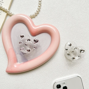 Detail of pink and silver heart-shaped gemstone phone grips on white textured background