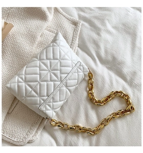 Detail of white quilted faux leather bag with chunky gold chain strap on tweed