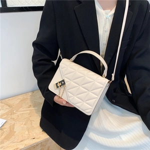 Minimalist beige quilted handbag with gold clasp and chain detail worn by a model