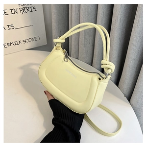 Detail of a creamy yellow half-moon baguette bag with a stylish knotted handle and metal zipper