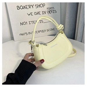 Detail of light yellow hobo bag featuring a knotted handle and silver chain accent