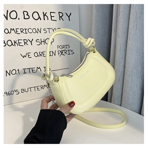 Detail of a creamy yellow crescent bag with knotted handle and silver fashion lettering
