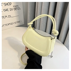Detail view of the artistic knotted handle and silver chain on this pale yellow handbag