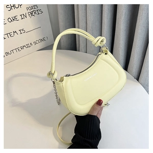 Detail of a creamy yellow half-moon leather bag with knotted handle and silver chain strap