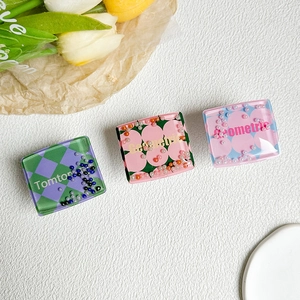Close-up of three square resin phone grips with floral, checkered, and polka dot sand patterns