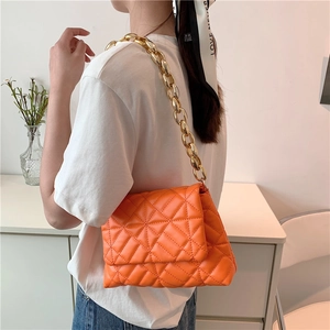 Orange quilted shoulder bag with gold chunky chain strap shown on model's shoulder