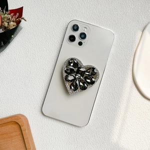 Detail shot of heart-shaped phone grip with luxury rhinestones on white smartphone