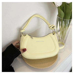Detail of pale yellow crescent handbag with woven handle and silver chain ornament