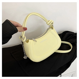 Detail of light lemon yellow crescent bag with knotted handle and metal chain decoration