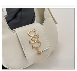 Detail of white half-moon bag featuring gold double-S logo and metallic tassel