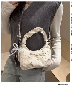 Detail of ruched crescent bag with sequin fabric, bow detail, and pearl charms