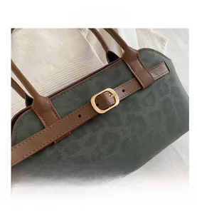 Detail of dark green suede handbag with brown leather straps and gold metal buckles