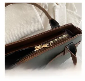 Detail of smooth gold zipper on green shell-shaped shoulder bag with brown leather trim