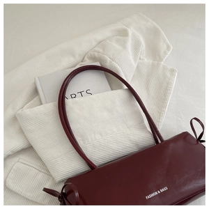 Close-up of burgundy matte leather baguette bag with strap knots and white lettering