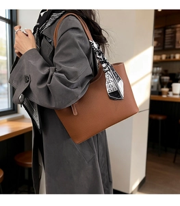 Close-up of brown litchi grain leather tote bag with a decorative silk scarf on handle
