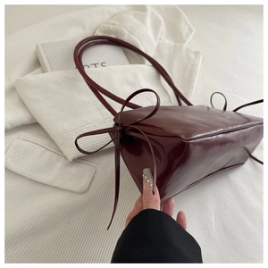 Detail view of burgundy glossy shoulder bag with minimalist side bow and double straps
