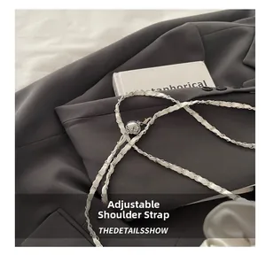 Detail of adjustable silver ball buckle and braided chain strap on white leather crescent bag